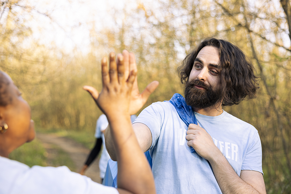 Male environmentalist sharing a high five with team members, enjoying successful activity to preserve the natural habitat. African american volunteer being pleased with a job well done.