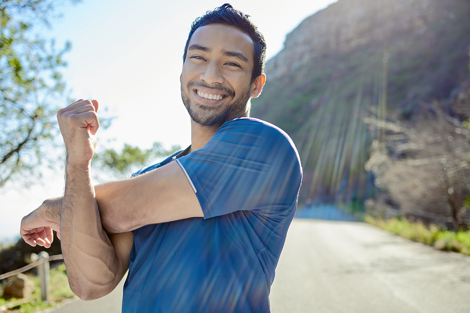 Shot of a handsome young man standing alone and stretching during his outdoor workout.