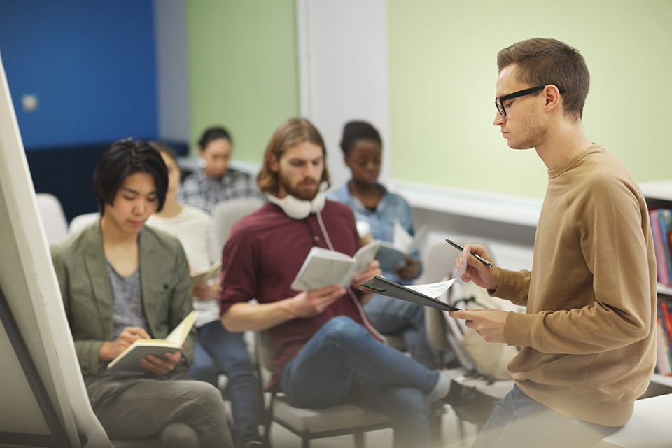 College student holding his report and presenting it to the audience while they making notes in notebooks